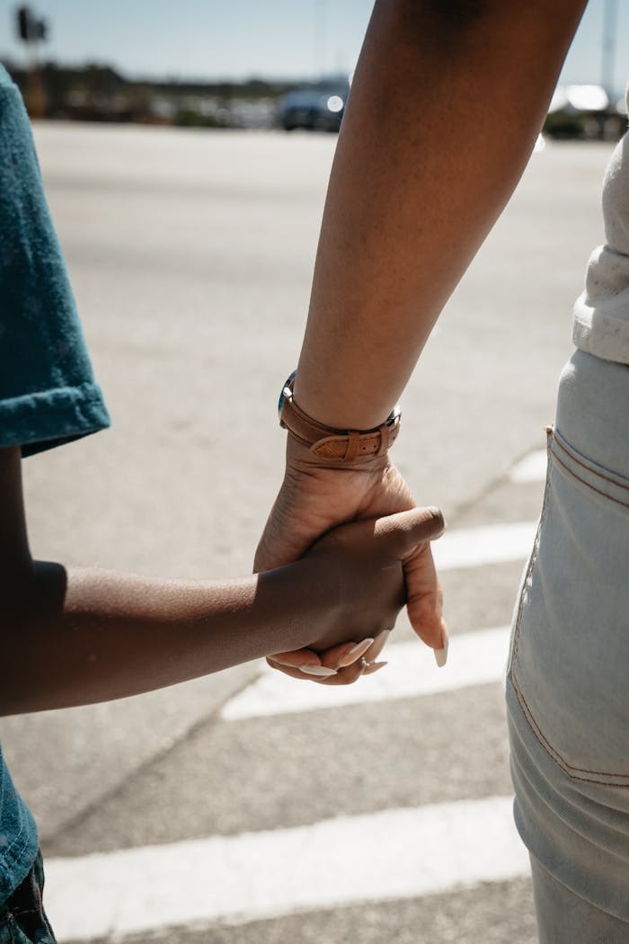 A mother and child holding hands, crossing a street safely on a zebra crossing.